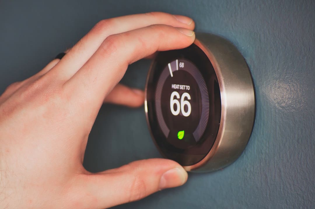 Hand operating smart thermostat to save money. Hand making adjustments by turning knob.