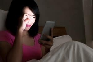 Woman on a bed in the dark staring sadly at a cell phone.
