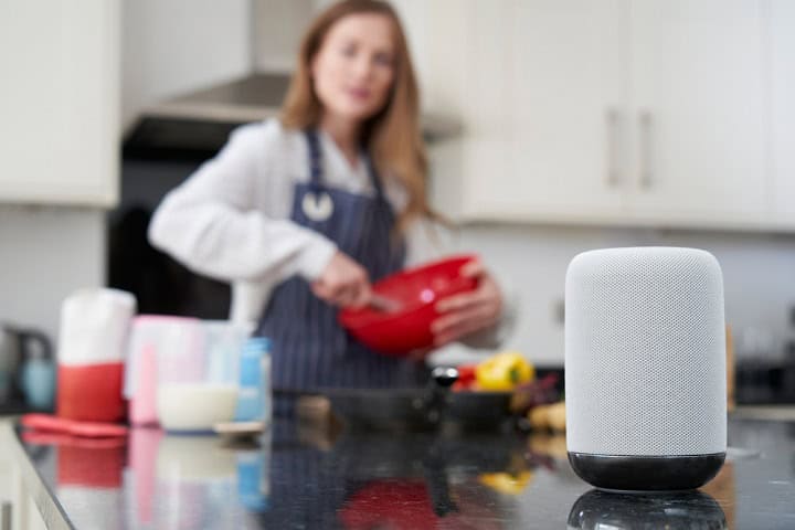 Woman cooking with smart speaker in foreground.