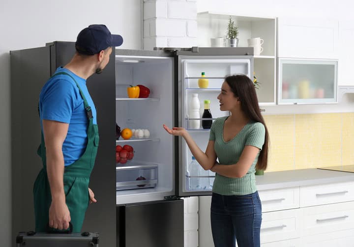 Refrigerator with repairman and client staring at it.