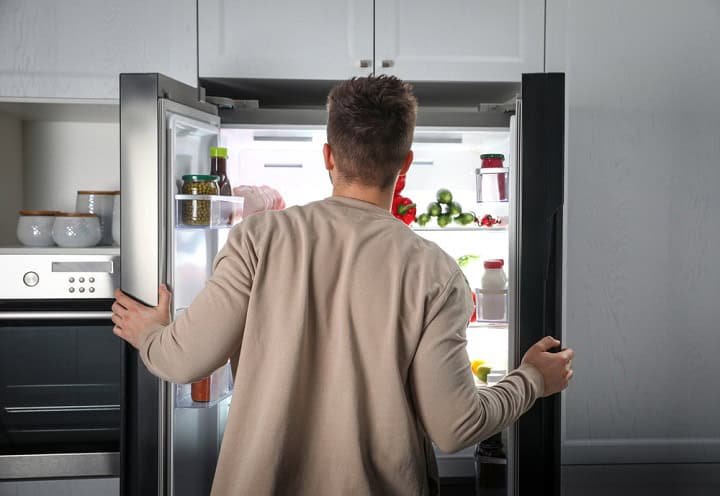 Young man opening refrigerator indoors, back view