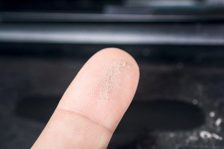 Close up of a finger with dust on it. Dusty device in the background.