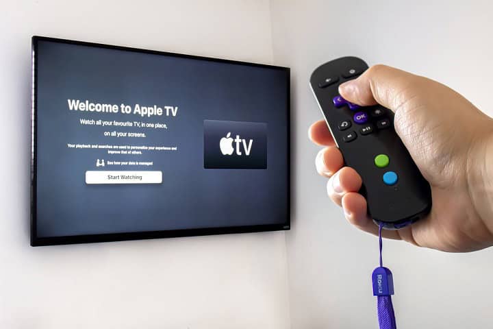 A person holding a Roku remote control with the apple tv application open a screen tv on the background