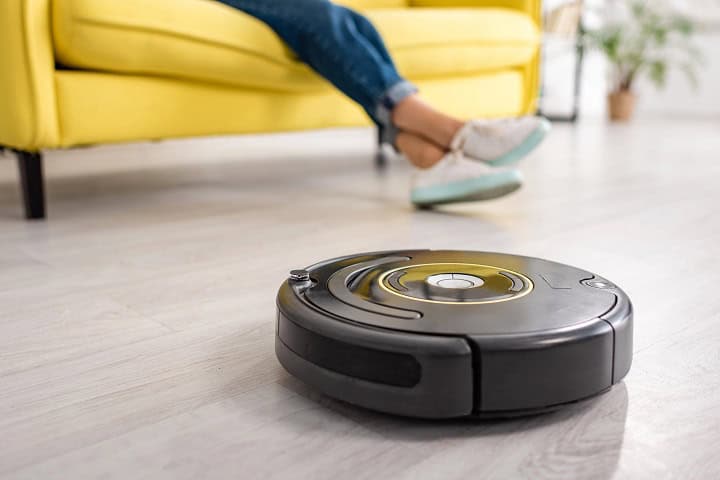 Robot vacuum cleaning the floor. Lower view of a person sitting on a couch in the background.